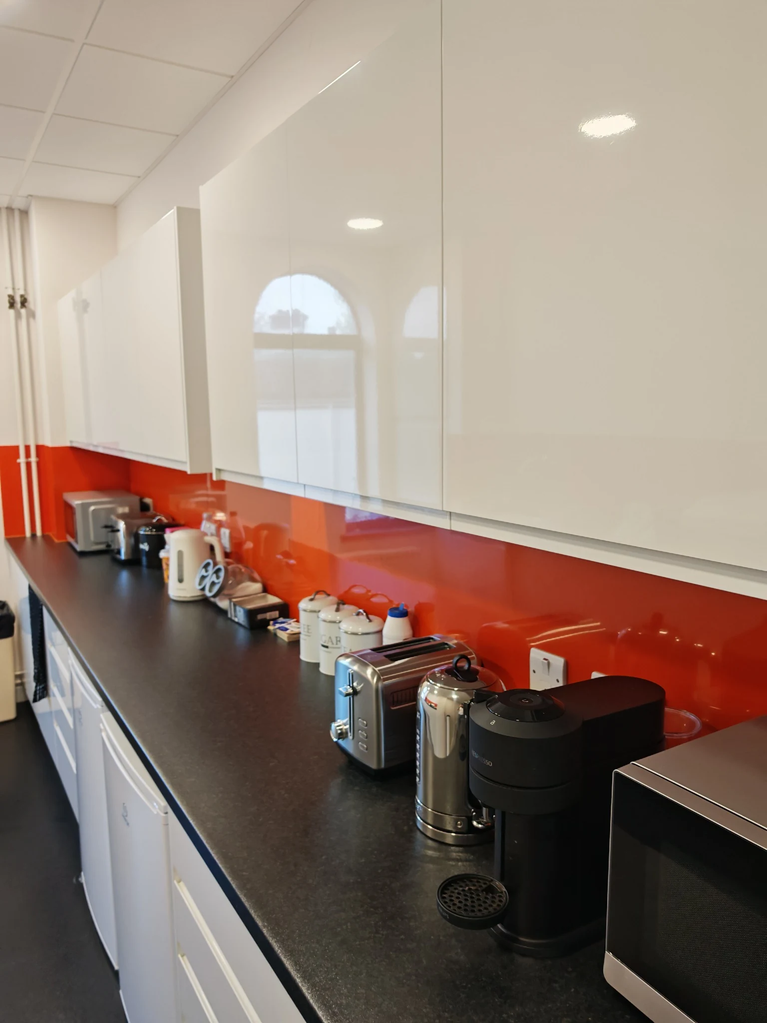 Clean office kitchen with red splashback